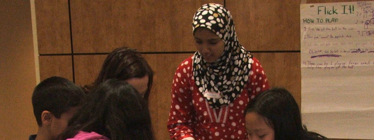 A woman in a headscarf and three children building a structure with plastic cups on a table during a science activity