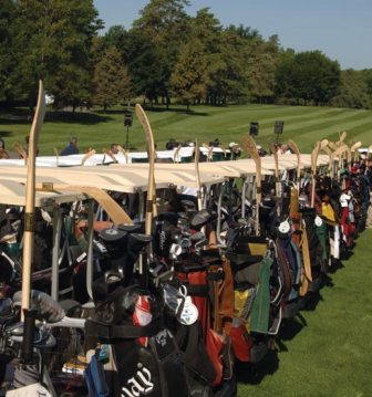 A long row of golf carts loaded with golf bags on a golf course lawn