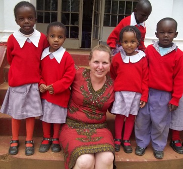 A woman in a red dress sitting on steps with five young children in red school uniforms