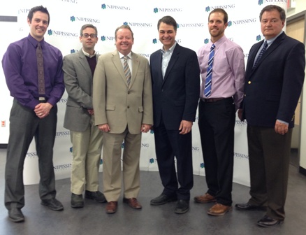 Six men in business clothes standing in a row in front of a Nipissing University backdrop