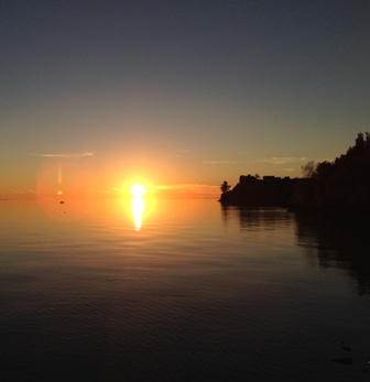 Sun setting over calm water, with a tree-covered point on the right