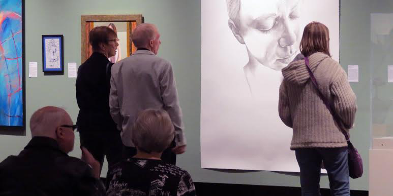 Visitors looking at a large charcoal portrait drawing hung in an art gallery