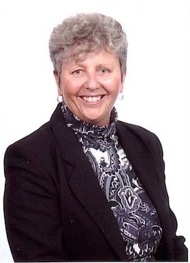 Portrait of a smiling woman with short grey curly hair wearing a black blazer and patterned scarf