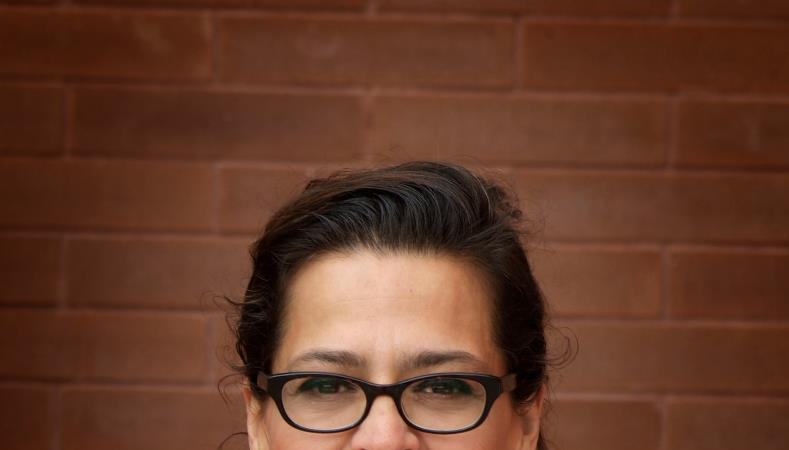 Portrait of a smiling woman with glasses wearing a red jacket in front of a brick wall