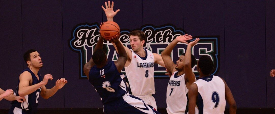 Nipissing Lakers basketball players in white defend as an opposing player in navy shoots near the basket