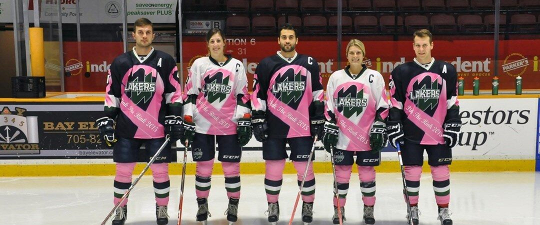 Five Nipissing Lakers hockey players in pink and green jerseys standing in a line on the ice