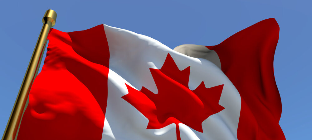The Canadian flag flapping in the wind against a blue sky