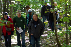 Adults and children walking single file along a wooded trail, holding trail maps
