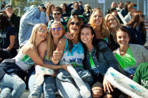Group of smiling students in Lakers shirts and sunglasses sitting together in the stands holding inflatable cheering sticks
