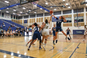 A Nipissing women's basketball player in a navy jersey stretches to shoot the ball over a defender during a game in the gym