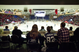 View from a stadium suite of spectators in Lakers jerseys watching a hockey game on the ice