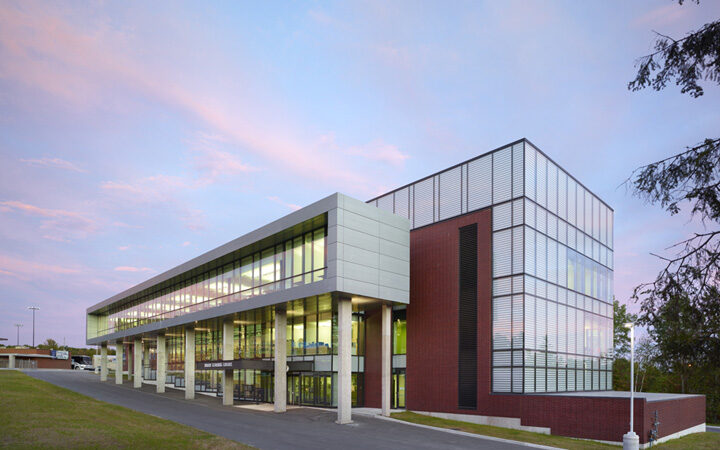 A modern three-storey brick and glass building at dusk with a covered walkway