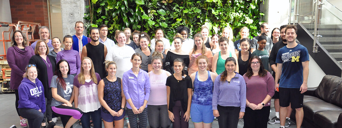 Large group of about fifty people kneeling and standing together for a group photo in a lobby with a living green wall