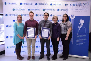 Five people pose in front of a Nipissing University backdrop and Dave Marshall Leadership Awards banner, two of them holding framed certificates