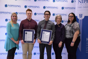 Five people pose in front of a Nipissing University backdrop and Dave Marshall Leadership Awards banner, two of them holding framed certificates