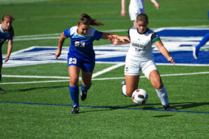 A Nipissing Lakers soccer player in white dribbles the ball past a defender in a blue number 23 jersey