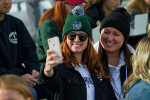 Two smiling women in Lakers toques take a selfie together in the stands
