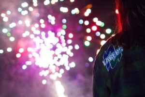 Colourful fireworks bursting in the night sky, seen over the shoulder of a person in a Lakers jacket