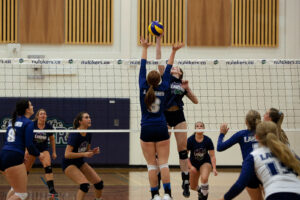 Nipissing women's volleyball players in navy jump at the net to block a spike during a match