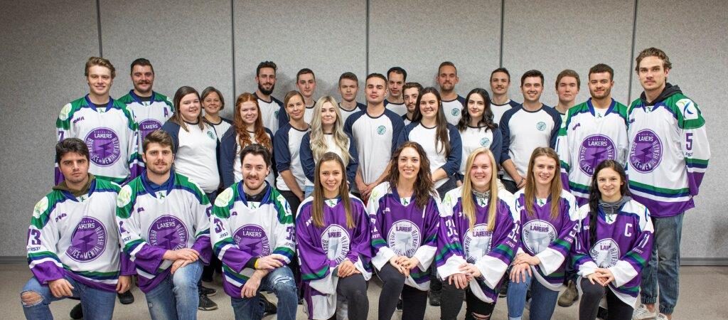 A team of about thirty hockey players, in white and purple jerseys, kneeling and standing together in rows for a group photo