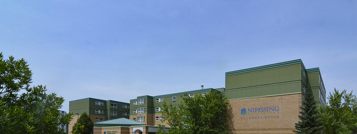 A brick and green-panelled residence building with a Nipissing University sign, with an empty parking lot in front