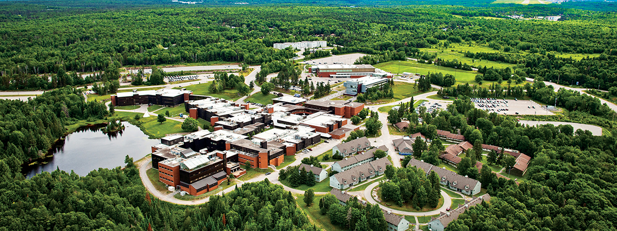 Aerial view of the Nipissing University campus surrounded by forest, with a small pond