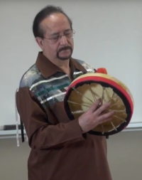 A man with glasses and a goatee holding a hand drum