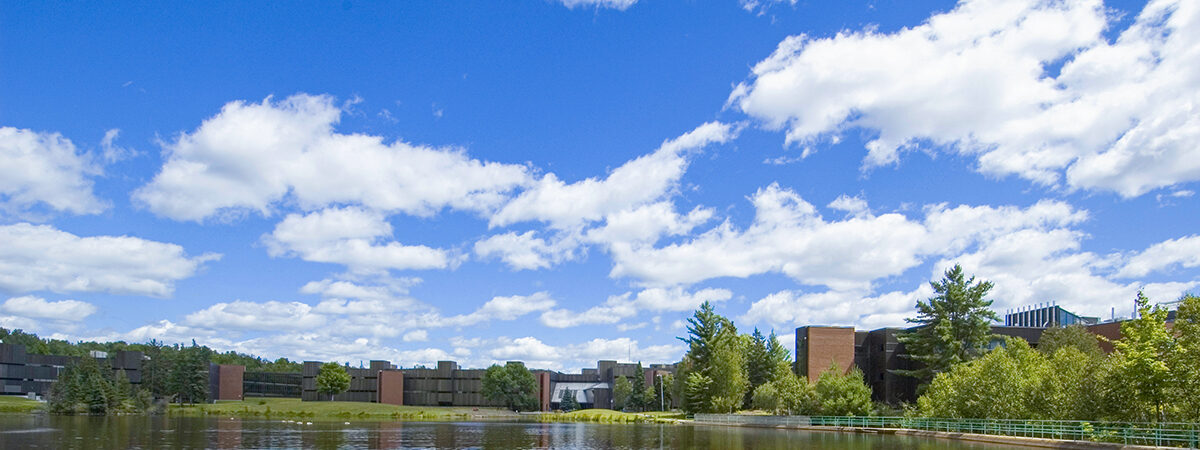 Clouds reflected in a pond with Nipissing University buildings on the far shore