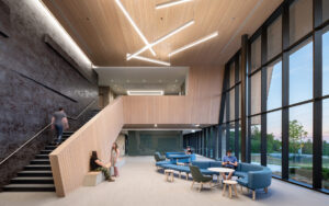 Bright two-storey atrium with a wooden staircase, floor-to-ceiling windows and blue lounge seating where people sit and talk