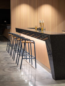 A wooden bar counter with beer taps and a row of tall stools in a modern lounge