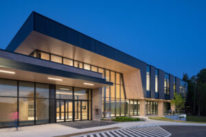 Modern two-storey building with a wood-panelled overhang and glass entrance at dusk