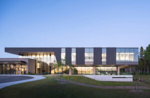 A modern two-storey building with dark panels and glass walls at dusk, with a sign at the front reading 'NUSU Student Centre'