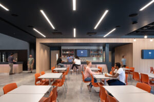 A modern café-style dining space with orange chairs, white tables and a bar in the background