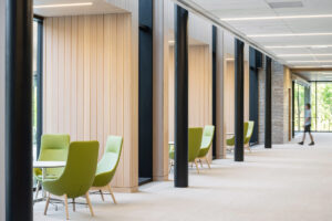 A bright hallway with wood-panelled walls and green armchairs beside tall windows