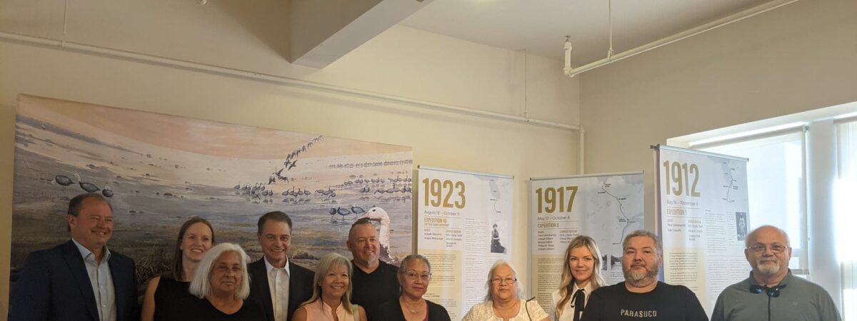 Ten people stand together behind a display case in front of historical timeline panels showing the years 1912, 1917 and 1923