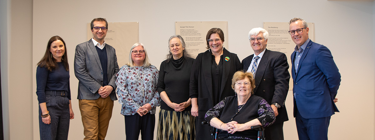 Seven people stand together in a gallery, with one woman seated in a wheelchair at the front