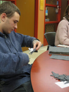 A man in a blue sweatshirt cutting grey felt at a table