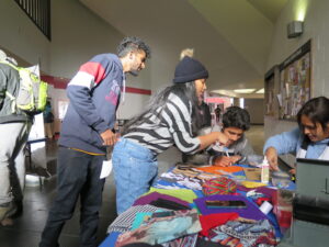 Students and staff gathered around a table covered in colourful fabric and craft materials in a university hallway