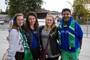 Four smiling people wearing Lakers and NUSU scarves and hoodies pose together outdoors