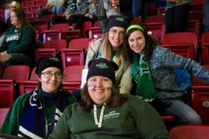 Four smiling fans in Lakers toques, scarves and sweatshirts sit together in red stadium seats