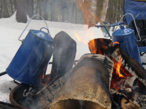 Two blue enamel coffee pots resting on a log fire in the snow