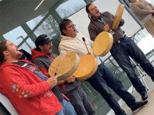 Four men in a hall singing and playing hand drums