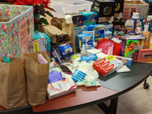 Boxes and paper bags on a table filled with donated toiletries and hygiene products, including toothpaste and pads