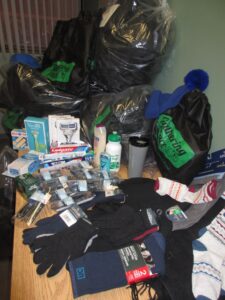 A table piled with donations of gloves, socks, toothpaste, razors and toiletries, with large black garbage bags behind