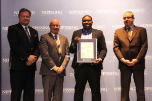 Dave Marshall Leadership Awards ceremony photo of an award recipient holding a framed certificate in front of a Nipissing University backdrop