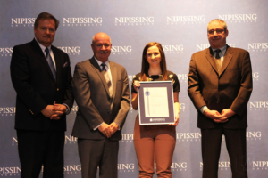 Dave Marshall Leadership Awards ceremony photo of an award recipient holding a framed certificate in front of a Nipissing University backdrop
