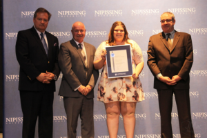 Dave Marshall Leadership Awards ceremony photo of an award recipient holding a framed certificate in front of a Nipissing University backdrop