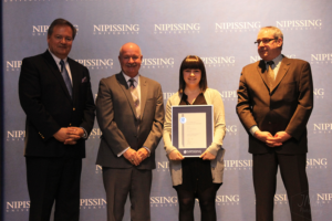 Dave Marshall Leadership Awards ceremony photo of an award recipient holding a framed certificate in front of a Nipissing University backdrop