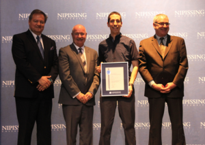 Dave Marshall Leadership Awards ceremony photo of an award recipient holding a framed certificate in front of a Nipissing University backdrop