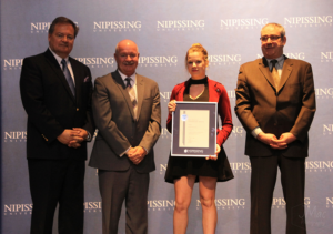 Dave Marshall Leadership Awards ceremony photo of an award recipient holding a framed certificate in front of a Nipissing University backdrop